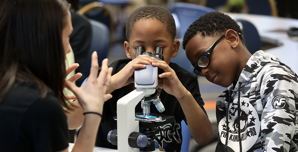 Two kids looking through a scope during one of the research events on campus.